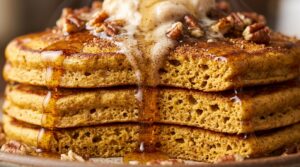 Ultra close-up macro of tall fluffy spiced pumpkin pancakes stacked high with melting butter and glistening pure maple syrup drip